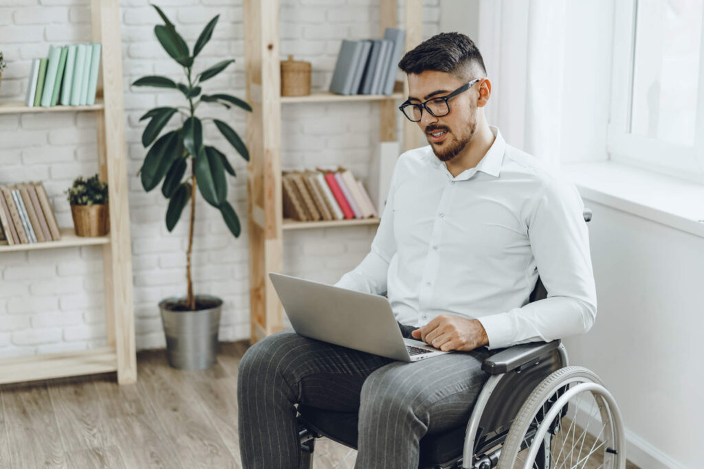 Man with glasses sitting in a wheelchair doing work on a laptop